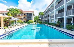 A rectangular swimming pool sits between two multi-story apartment buildings with palm trees — 601 Pine Drive # 207, Pompano Beach FL 33060, POMPANO BEACH, FL