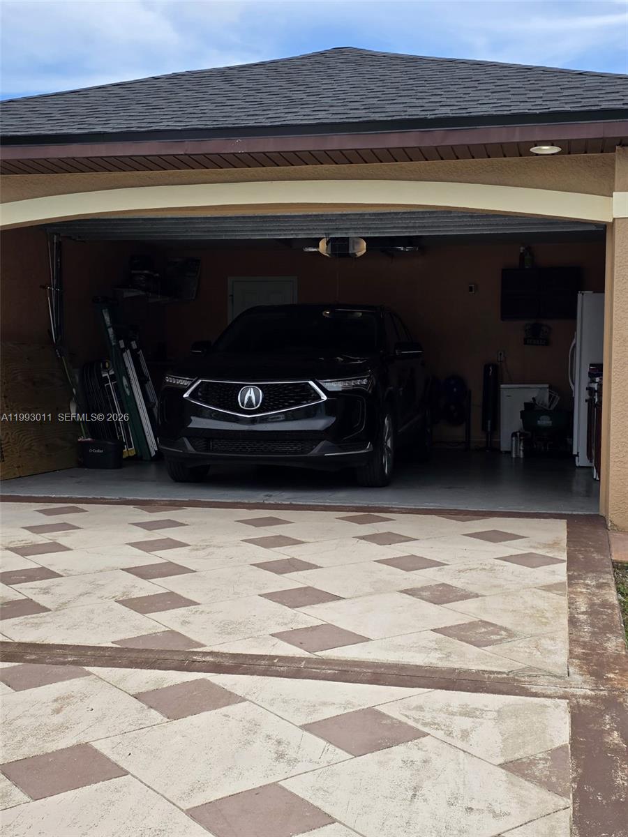 A black Acura SUV is parked inside a residential garage with a patterned concrete driveway — 1816 Tomaso Ave, Lehigh Acres FL 33972, LEHIGH ACRES, FL