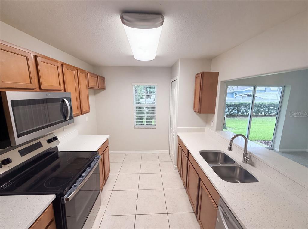 A kitchen features wood cabinets, white countertops, stainless steel appliances, and tile flooring — 37557 DALIHA TERRACE, ZEPHYRHILLS, FL