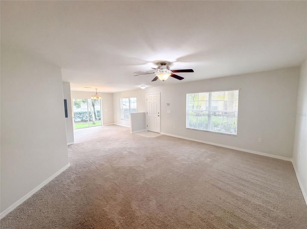 A spacious living room features beige carpeting, a ceiling fan, and large windows — 37557 DALIHA TERRACE, ZEPHYRHILLS, FL