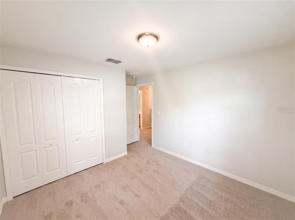 A bedroom with beige carpet, white walls, a white closet, and a doorway to another room — 37557 DALIHA TERRACE, ZEPHYRHILLS, FL