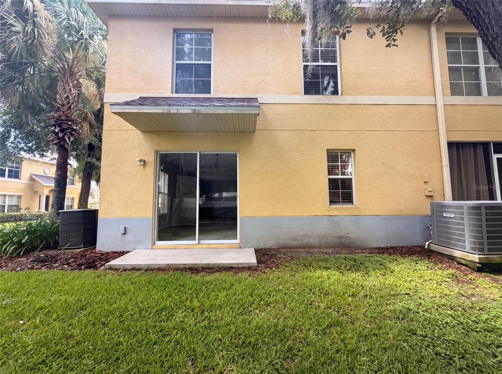 The exterior of a two-story yellow stucco building features a sliding glass door and patio — 37557 DALIHA TERRACE, ZEPHYRHILLS, FL