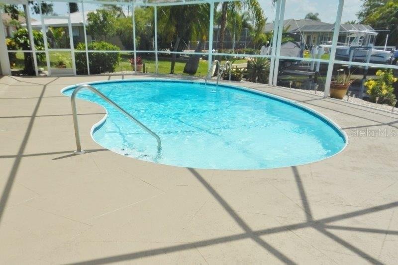 A kidney-shaped swimming pool sits on a concrete patio enclosed by a screened lanai — 910 SANTA BRIGIDA COURT, PUNTA GORDA, FL