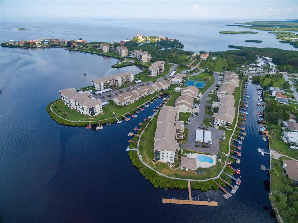 An aerial view shows a waterfront condominium complex with boat docks, a pool, and tennis courts — 8211 BRENT STREET UNIT 816, PORT RICHEY, FL
