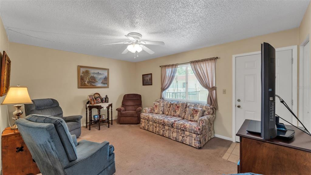 A living room features a floral sofa, two recliners, a television, and beige carpeting — 1130 N LAKE PARKER AVENUE UNIT C321, LAKELAND, FL