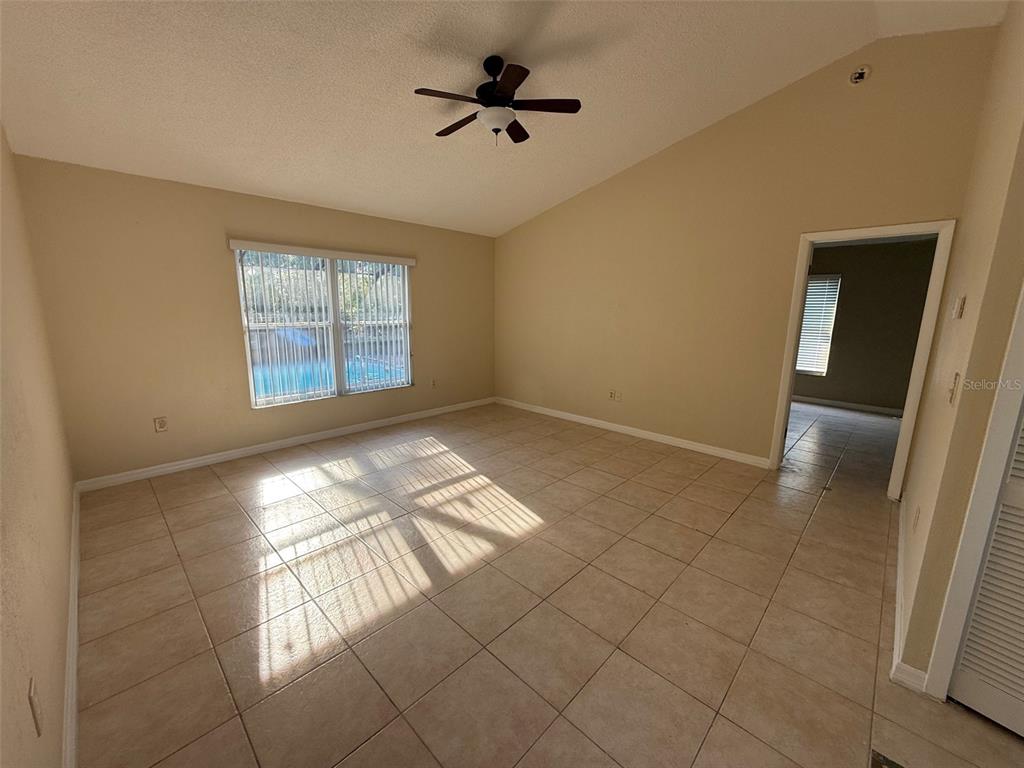 An empty room with beige tile flooring, a vaulted ceiling, and a ceiling fan — 2392 FAIRVIEW ROAD, SPRING HILL, FL