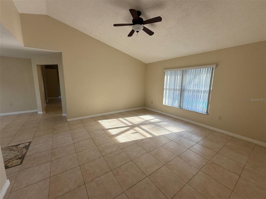An empty living room features a vaulted ceiling, a ceiling fan, and beige tile flooring — 2392 FAIRVIEW ROAD, SPRING HILL, FL