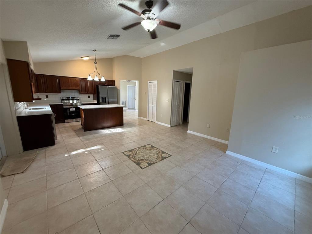 A kitchen with dark wood cabinets and an island opens into a tiled living area — 2392 FAIRVIEW ROAD, SPRING HILL, FL