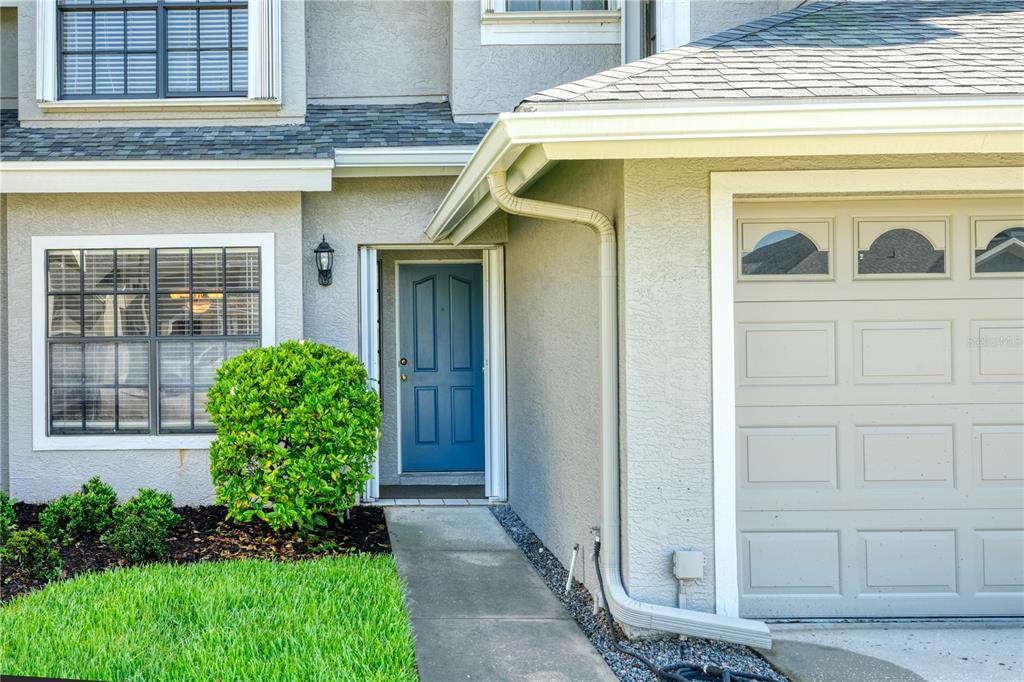A blue front door is situated next to a beige garage door and a landscaped yard — 12709 BURMAH COURT, ODESSA, FL