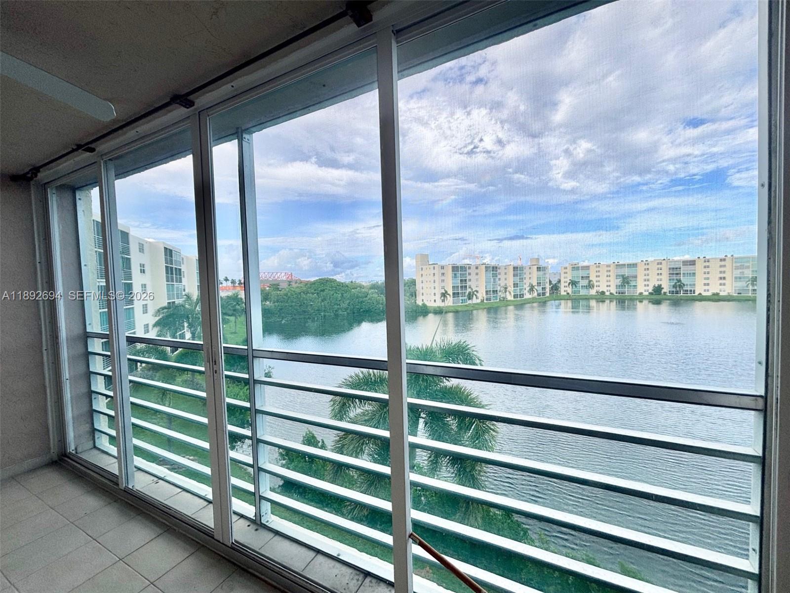 A balcony with tiled flooring and metal railings overlooks a lake and apartment buildings — 141 SE 3rd Ave # 402, Dania Beach FL 33004, DANIA BEACH, FL