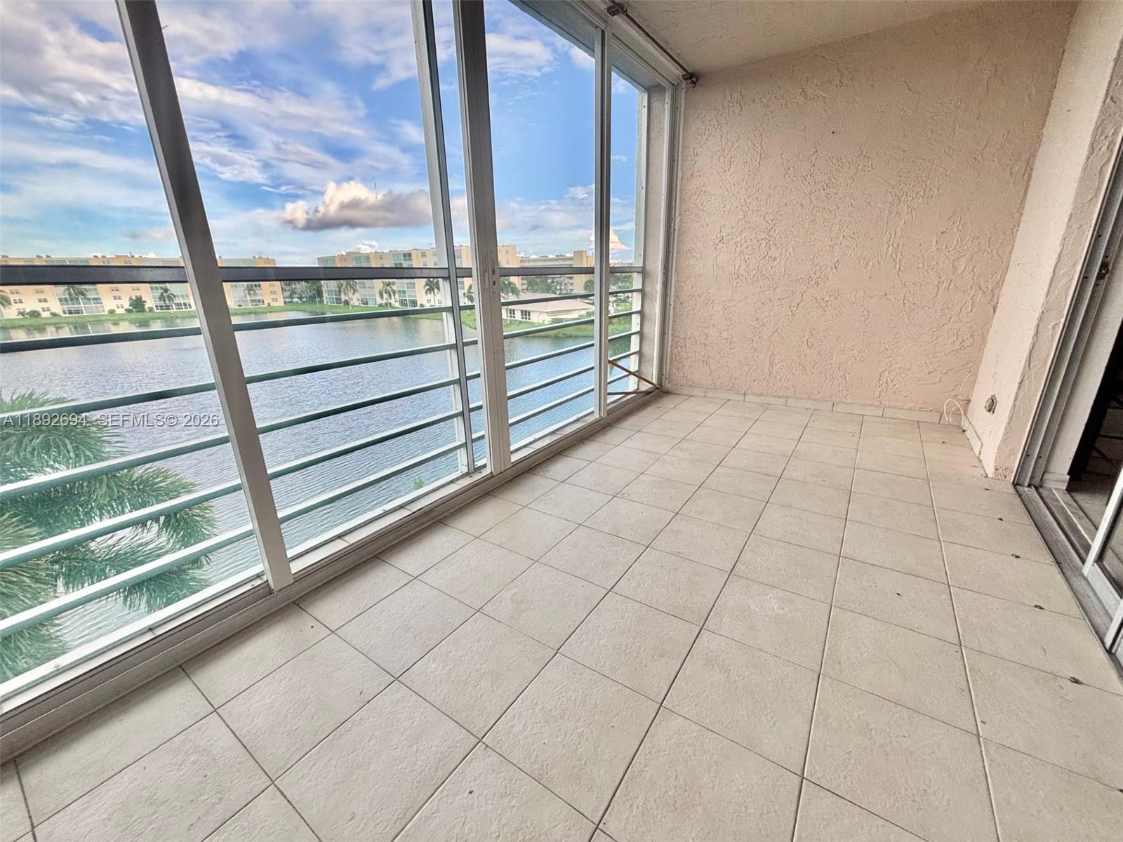 A balcony with light-colored tile flooring, enclosed by glass windows overlooking a lake — 141 SE 3rd Ave # 402, Dania Beach FL 33004, DANIA BEACH, FL