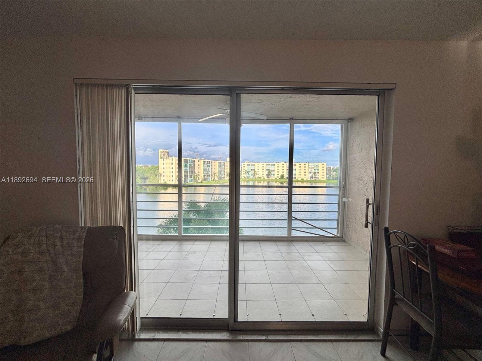 A view of a tiled balcony overlooking a lake and apartment buildings through sliding doors — 141 SE 3rd Ave # 402, Dania Beach FL 33004, DANIA BEACH, FL