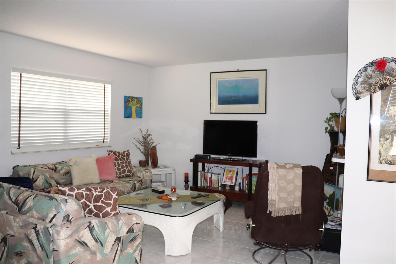A living room features a patterned sofa, a glass coffee table, and a television console — 26 Brittany # A, Delray Beach FL 33446, DELRAY BEACH, FL