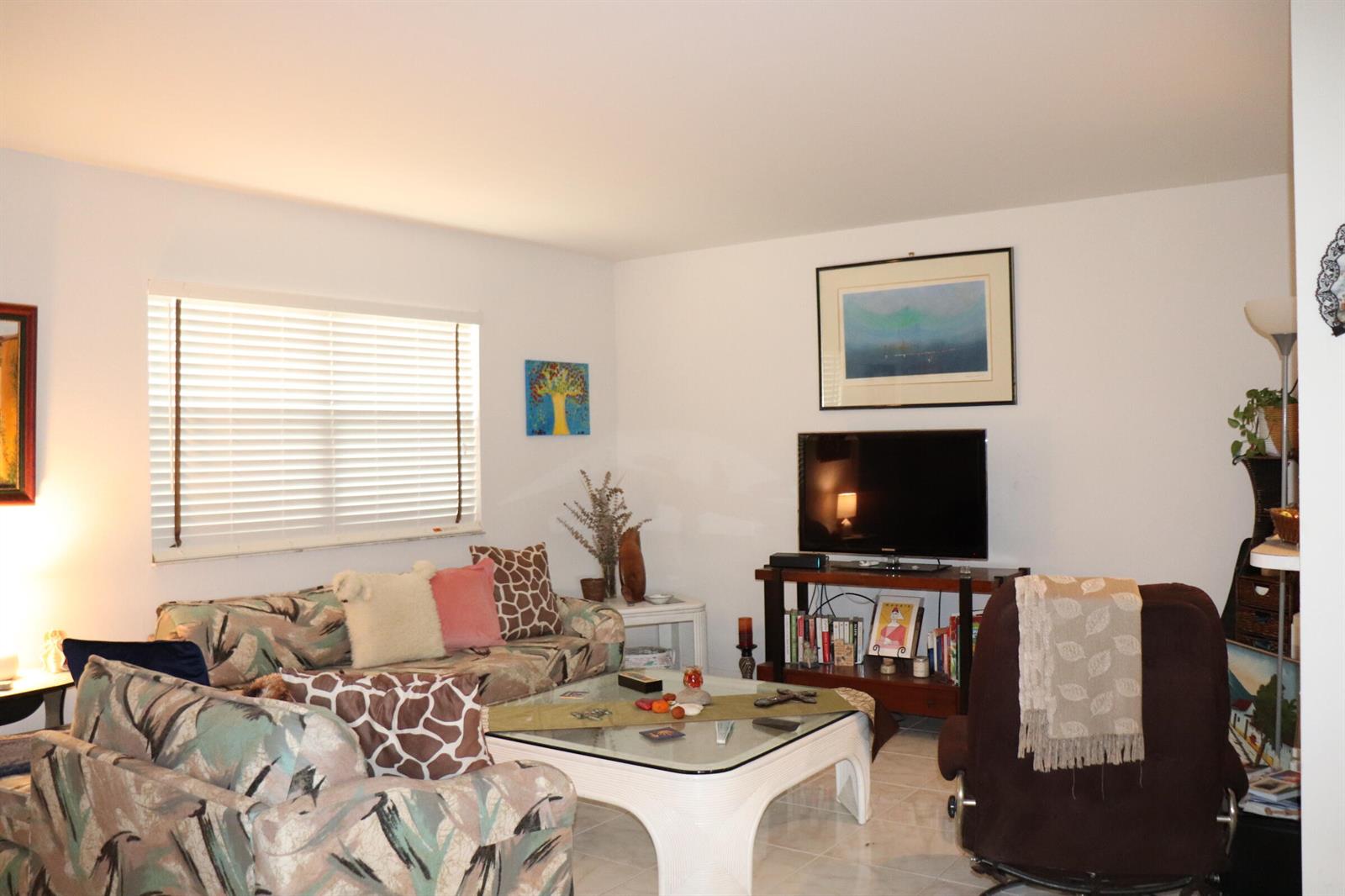 A living room features a patterned sofa, a glass coffee table, and a television stand — 26 Brittany # A, Delray Beach FL 33446, DELRAY BEACH, FL