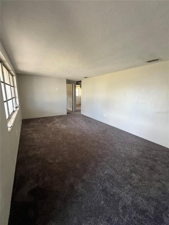 An empty room features dark gray carpeting, light-colored walls, and a window on the left — 4144 KIBLER LANE, HOLIDAY, FL