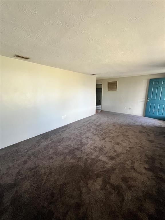 An empty room with dark gray carpeting, light-colored walls, and a blue entry door — 4144 KIBLER LANE, HOLIDAY, FL