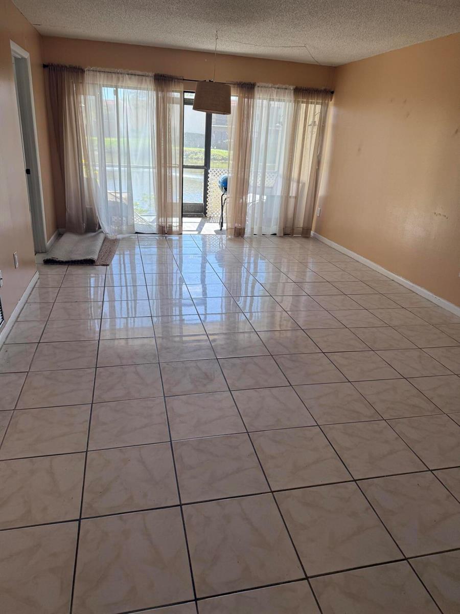 An empty room with beige tile flooring, peach walls, and large sliding glass doors — 2025 Oleander Boulevard # 105, Fort Pierce FL 34982, FORT PIERCE, FL