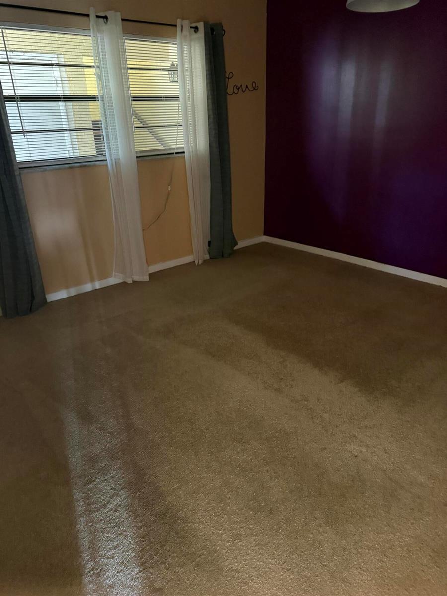 An empty bedroom features tan carpet, a purple accent wall, and windows with curtains — 2025 Oleander Boulevard # 105, Fort Pierce FL 34982, FORT PIERCE, FL