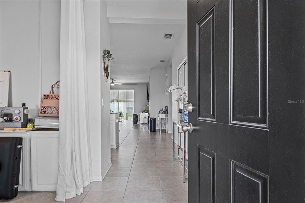 A view from an open black door into a tiled hallway leading to a living area — 2621 GLENROCK COURT, KISSIMMEE, FL