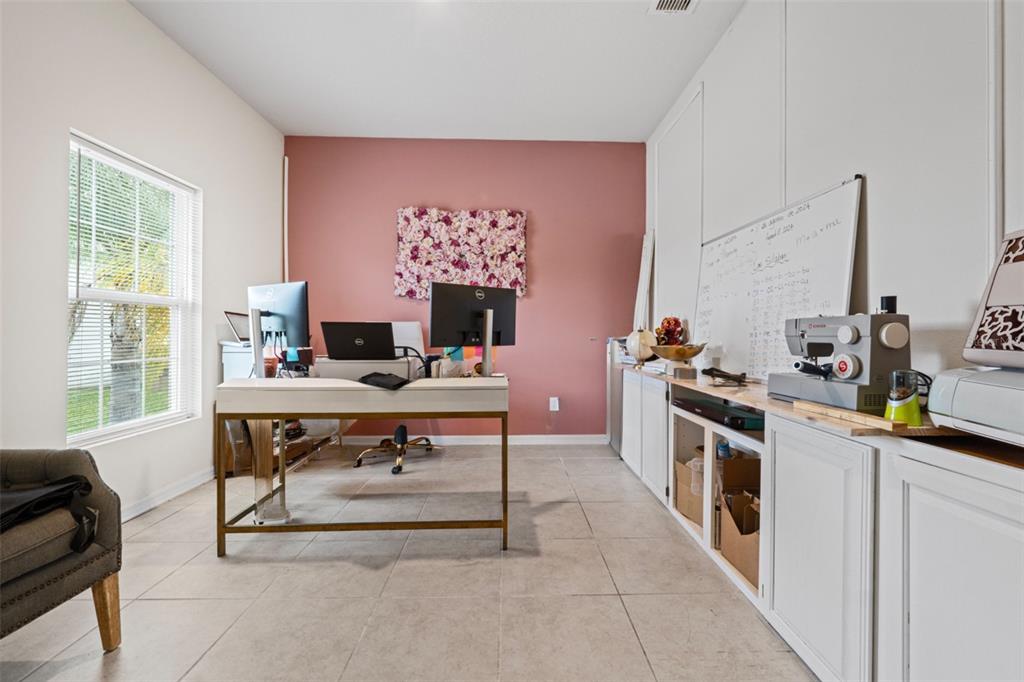 A home office features a pink accent wall, a desk, built-in cabinets, and tile flooring — 2621 GLENROCK COURT, KISSIMMEE, FL