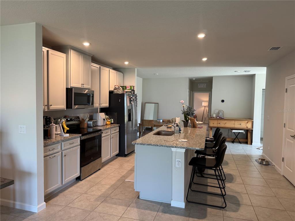 A kitchen features white cabinets, granite countertops, a central island, and stainless steel appliances — 461 VOLTAIRE DRIVE, SPRING HILL, FL