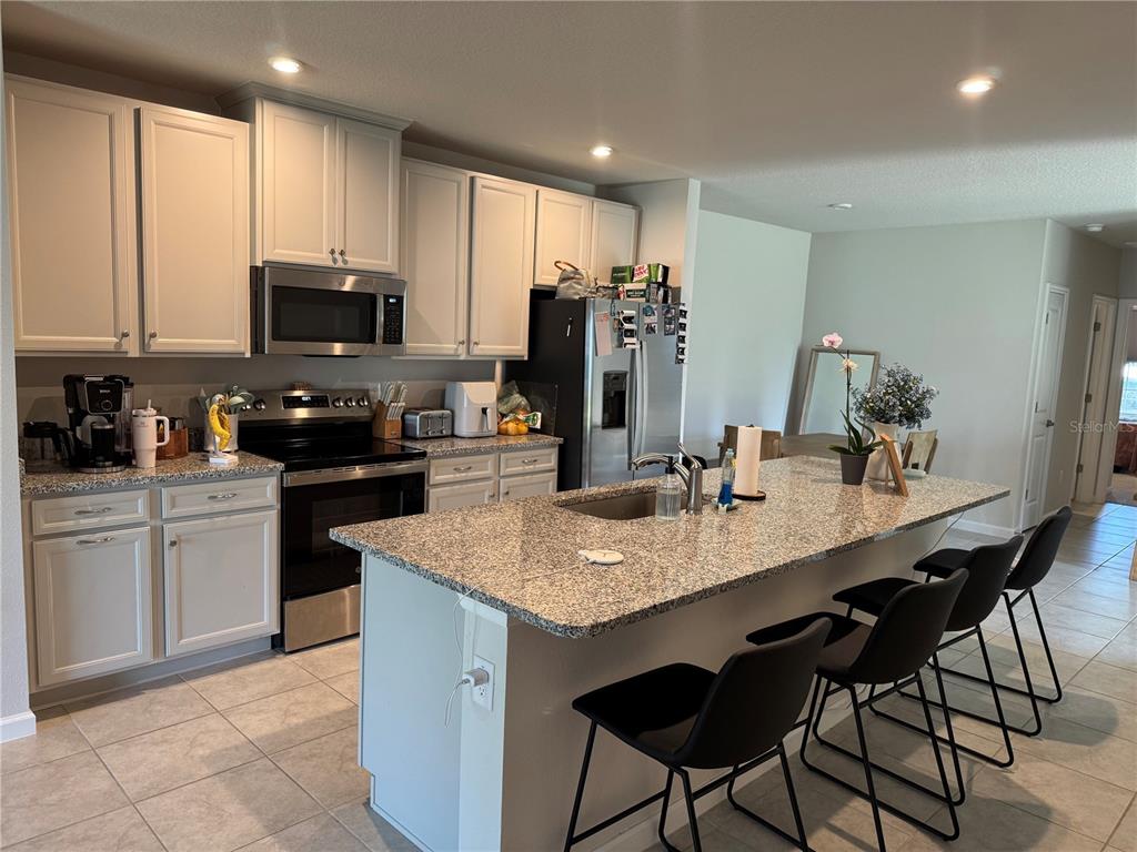A kitchen features light cabinets, granite countertops, a center island with seating, and stainless appliances — 461 VOLTAIRE DRIVE, SPRING HILL, FL