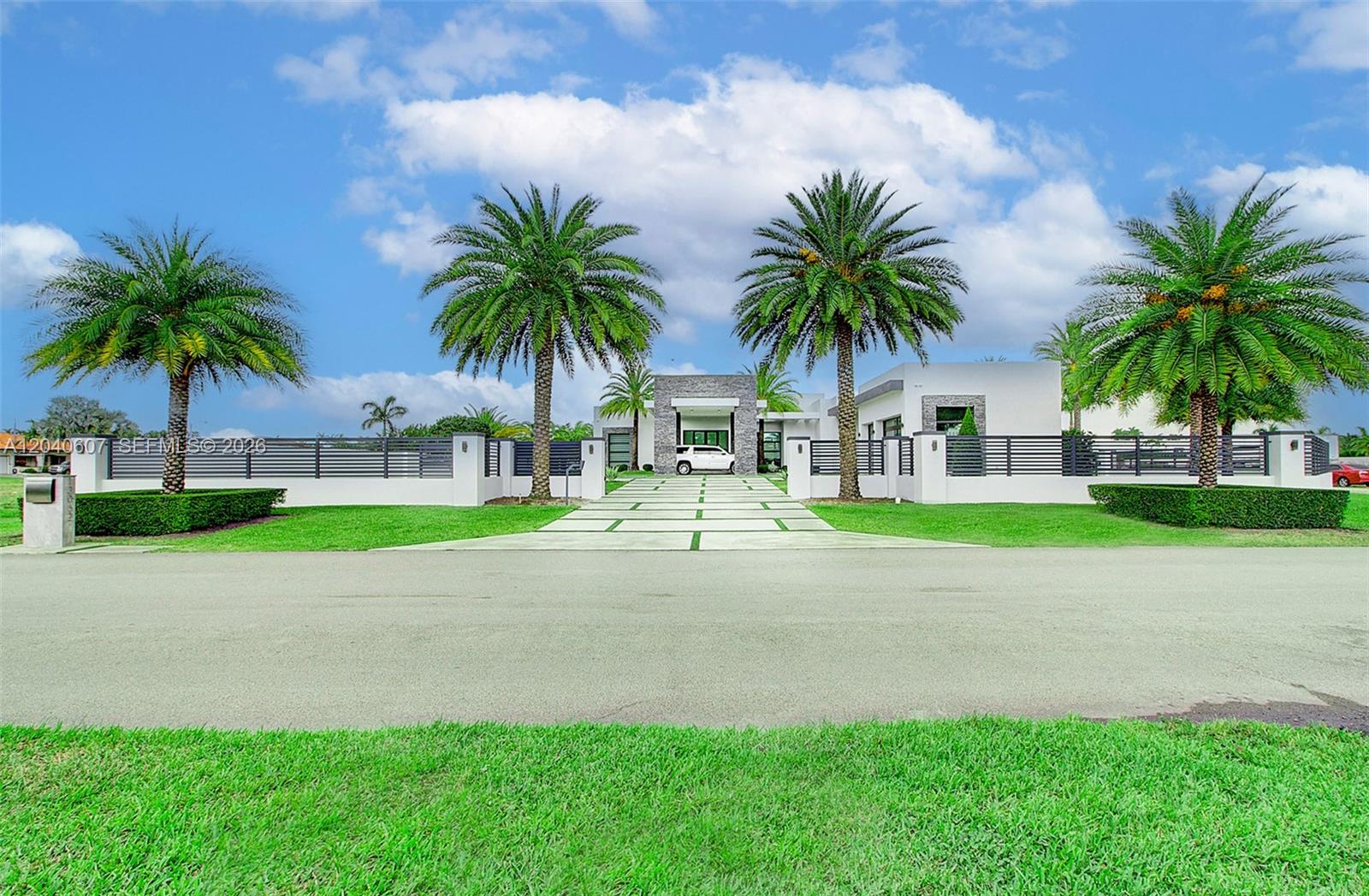 A modern white house with a stone entryway is framed by palm trees and fencing — 13052 NW 102nd Ave, Hialeah Gardens FL 33018, HIALEAH GARDENS, FL