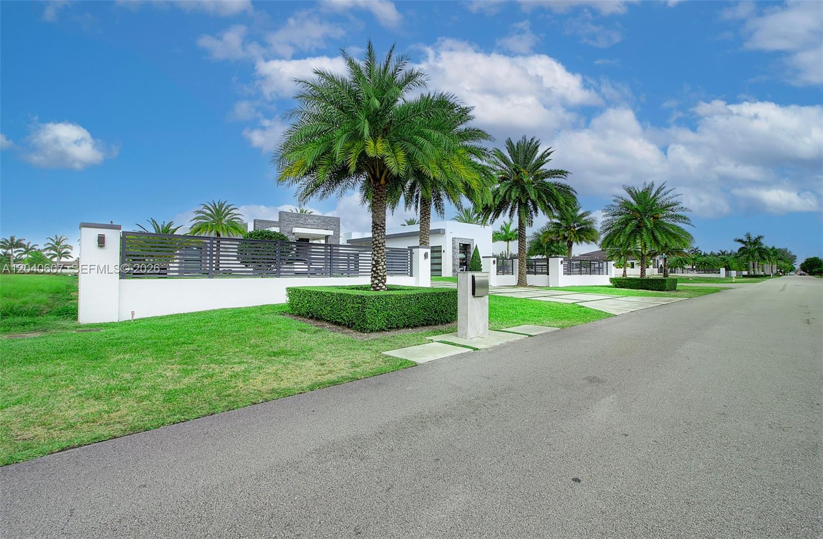 A modern white house with a gated entrance and palm trees sits along a street — 13052 NW 102nd Ave, Hialeah Gardens FL 33018, HIALEAH GARDENS, FL