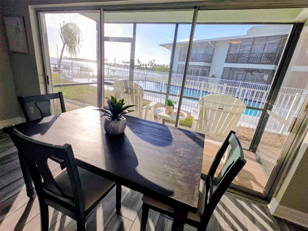A dining area with a dark wood table overlooks a patio, pool, and waterfront view — 2566 GARY CIRCLE UNIT 5, DUNEDIN, FL