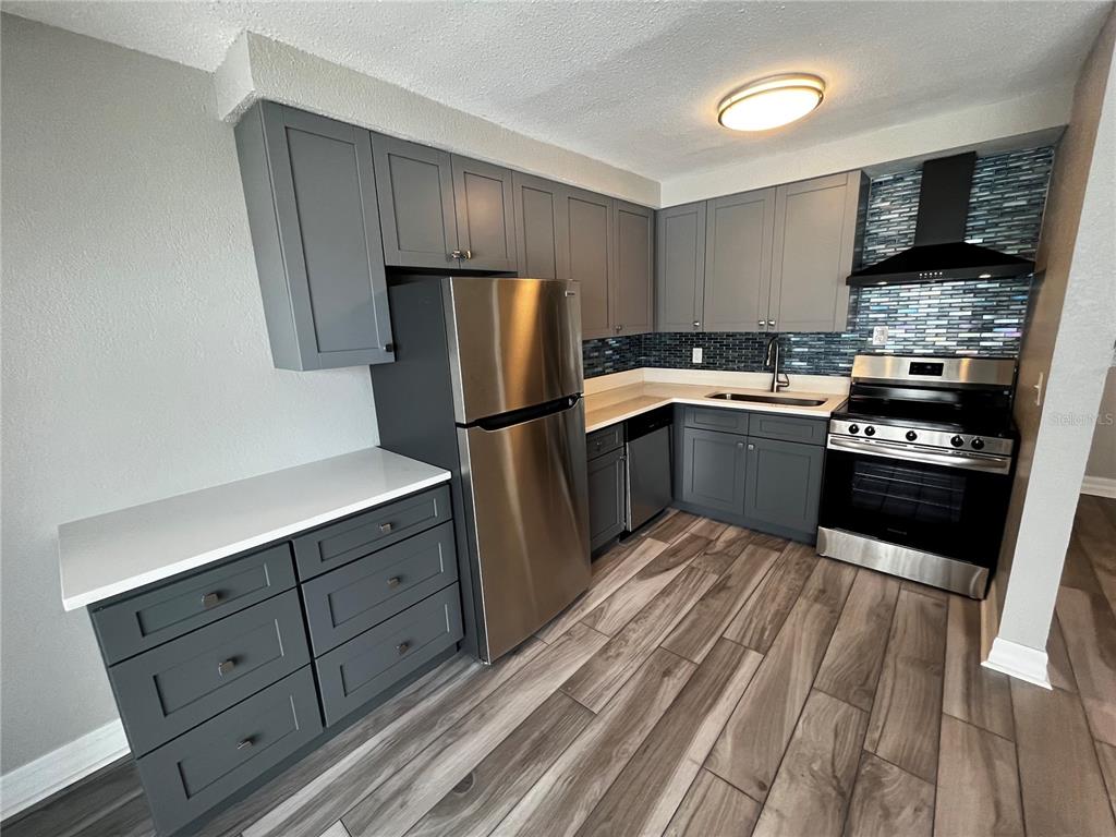 A kitchen features gray cabinets, stainless steel appliances, a tiled backsplash, and wood-look flooring — 2566 GARY CIRCLE UNIT 5, DUNEDIN, FL