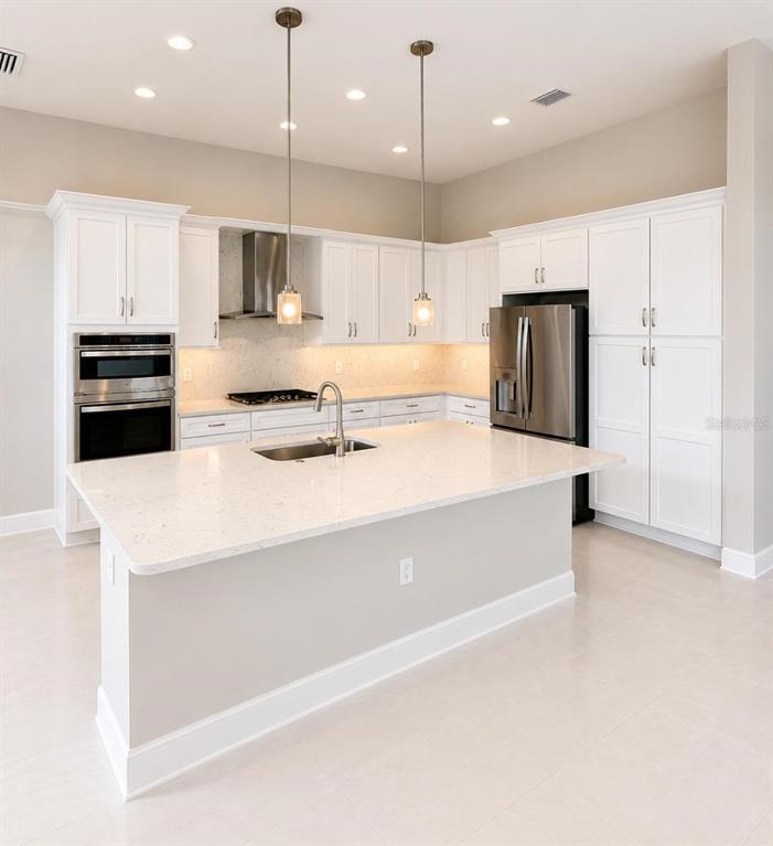 A modern kitchen features white cabinetry, stainless steel appliances, a large island, and pendant lighting — 32630 NEROLI STREET, WESLEY CHAPEL, FL