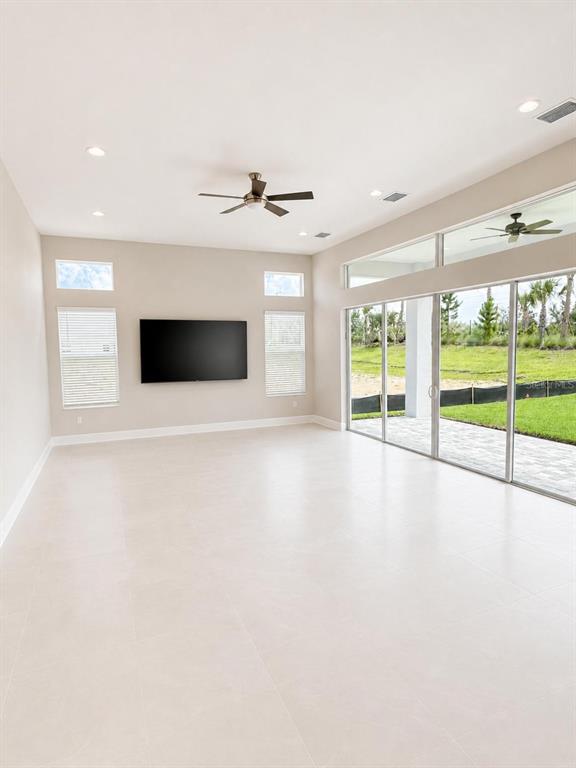 A bright living room features light tile floors, a wall-mounted television, and large sliding glass doors — 32630 NEROLI STREET, WESLEY CHAPEL, FL