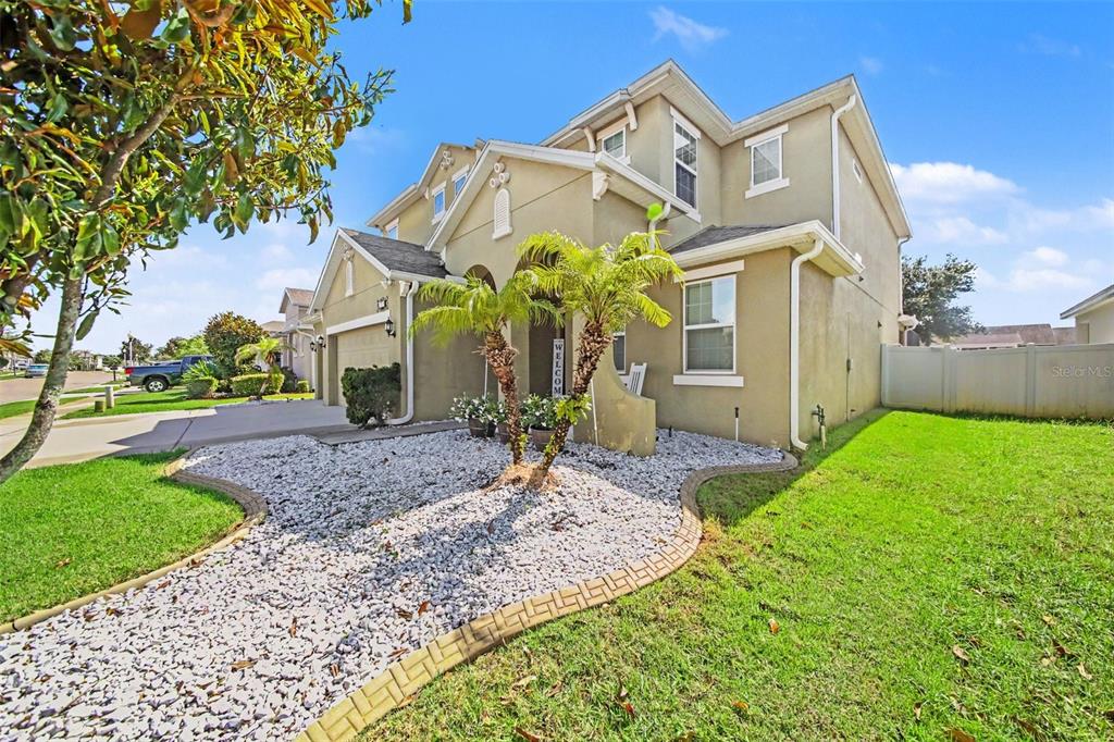 A two-story tan house with a gravel front yard, palm trees, and a paved driveway — 1374 MERION DRIVE, MOUNT DORA, FL