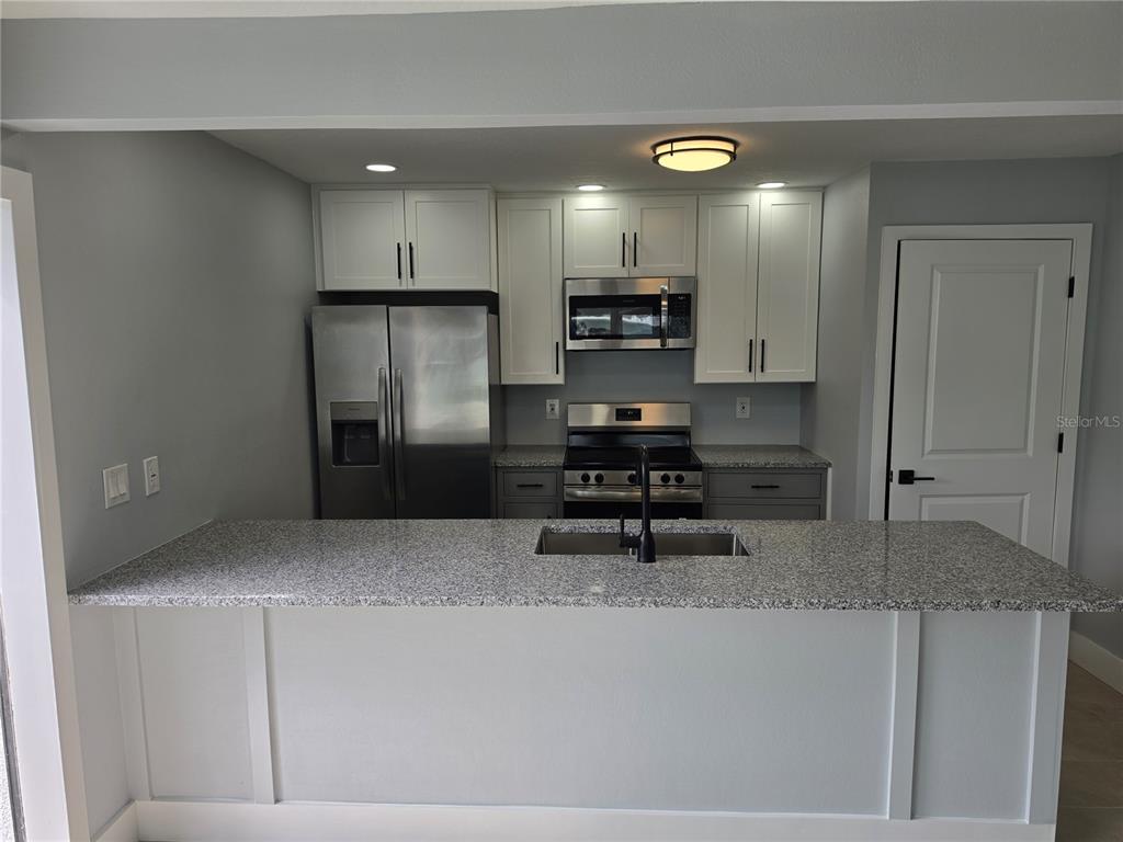 A kitchen features a granite-topped island, stainless steel appliances, and white cabinetry — 145 131ST AVENUE E UNIT 3, ST PETERSBURG, FL