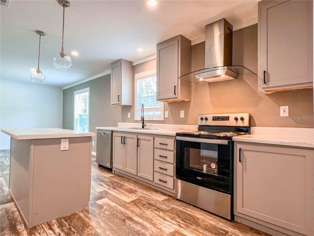 A kitchen features gray cabinets, stainless steel appliances, a kitchen island, and wood-look flooring — 16108 GUPTON STREET, BROOKSVILLE, FL