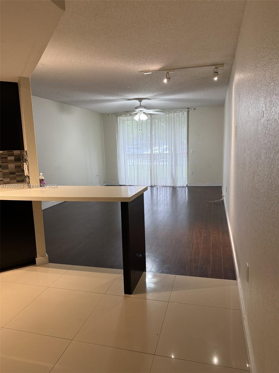 A kitchen counter overlooks a living area with dark wood flooring and sliding glass doors — 8225 Lake Dr # 107, Doral FL 33166, DORAL, FL
