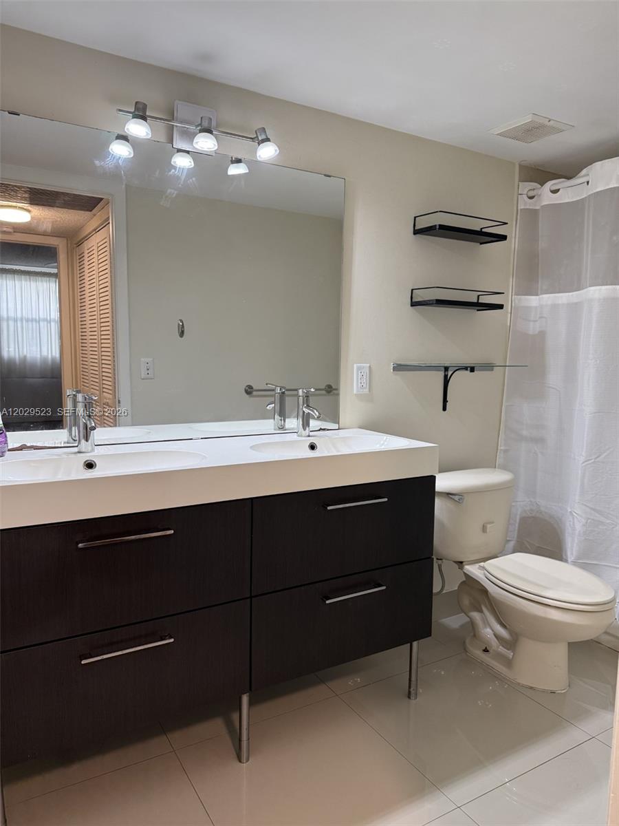 A bathroom features a double-sink vanity with dark cabinets, a large mirror, and a toilet — 8225 Lake Dr # 107, Doral FL 33166, DORAL, FL