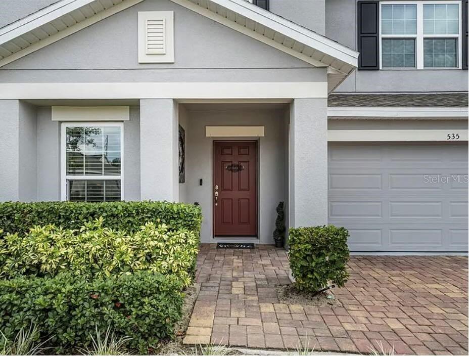 A gray house exterior features a red front door, a paved walkway, and manicured hedges — 535 DARSHIRE AVENUE, EUSTIS, FL