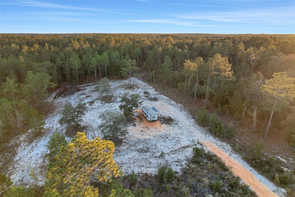 An aerial view shows a travel trailer parked on a cleared, sandy lot amidst woods — 161 WINDY HILLS ROAD, HAWTHORNE, FL