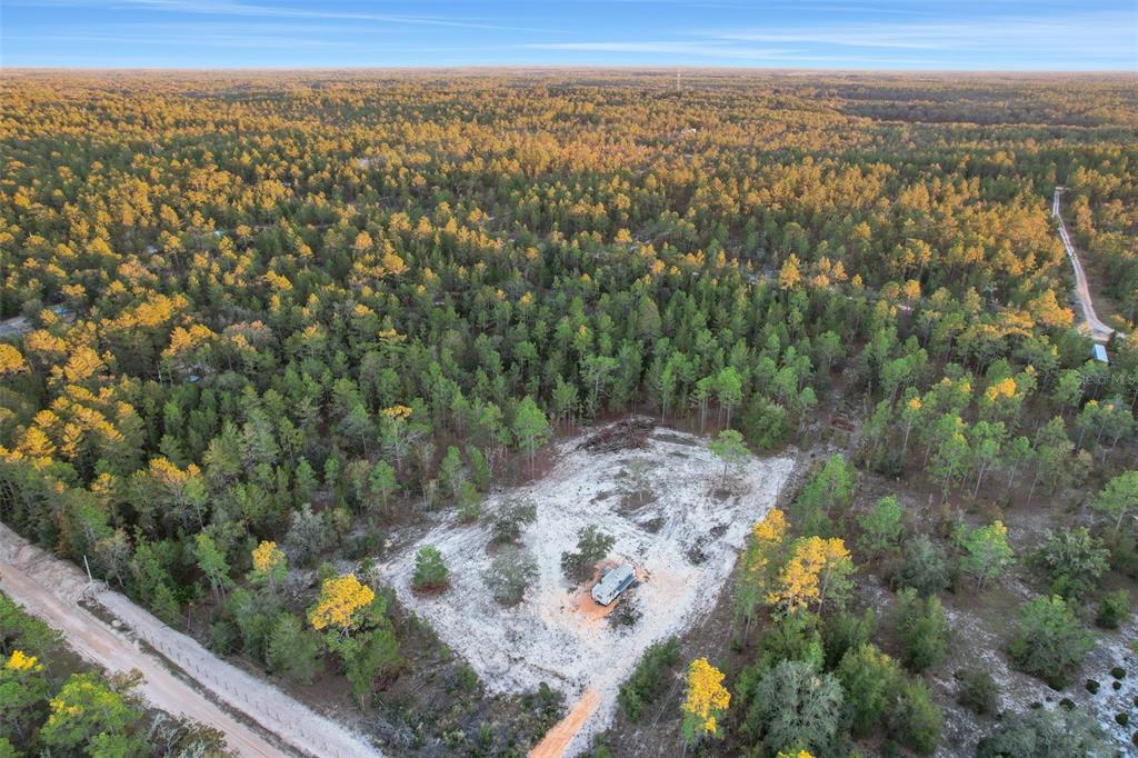 An aerial view shows a small camper parked on a cleared sandy lot amidst forest — 161 WINDY HILLS ROAD, HAWTHORNE, FL
