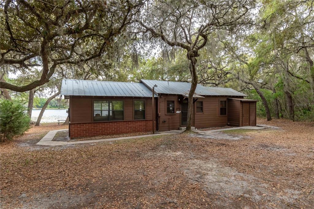 A brown wooden cabin with a metal roof sits among trees near a lake — 22645 NE 105TH AVENUE ROAD, FORT MC COY, FL