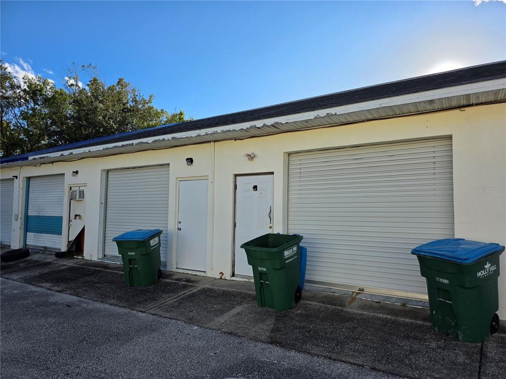 An exterior view of a commercial building featuring multiple roll-up garage doors and entry doors — 787 CENTER STREET UNIT H, HOLLY HILL, FL