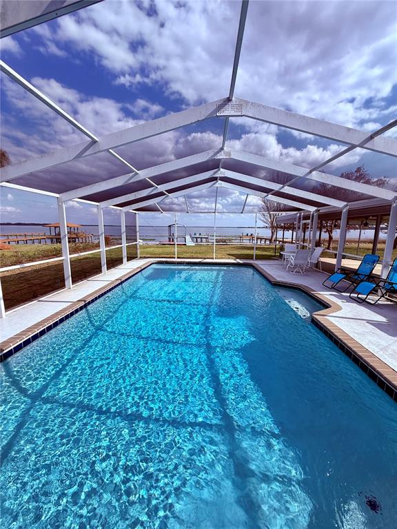 A large grassy backyard features a screened-in pool enclosure and a detached metal carport — 148 N LAKE REEDY BOULEVARD, FROSTPROOF, FL