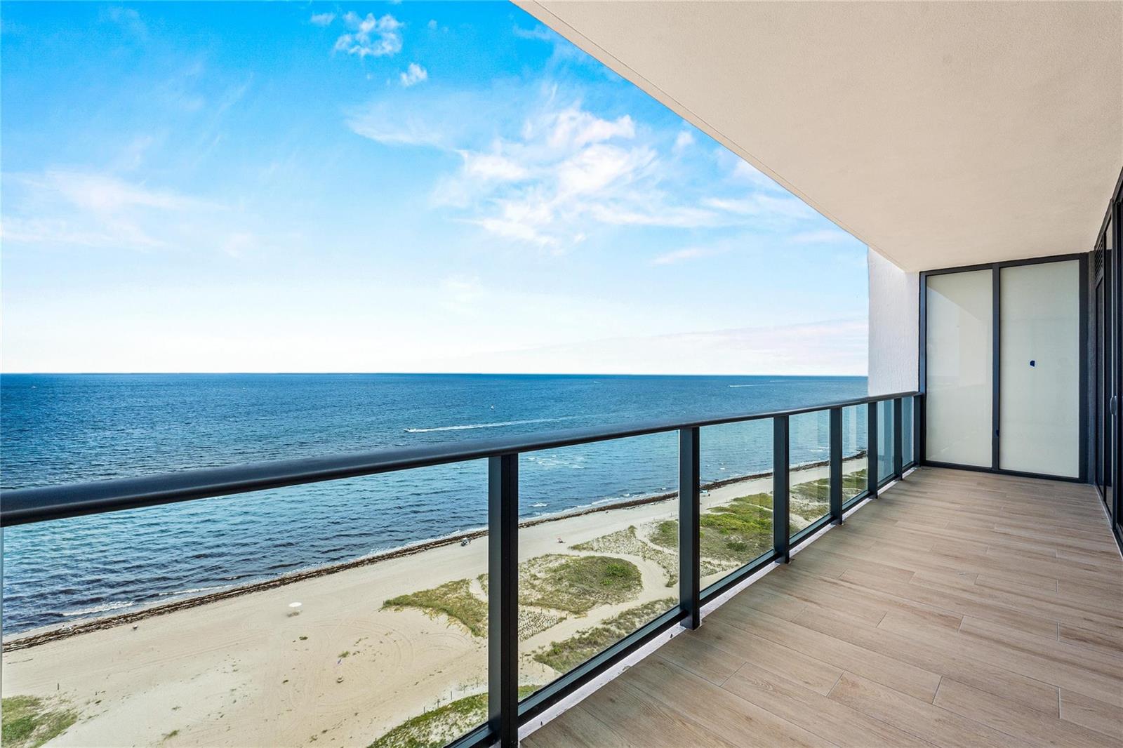 A balcony with wood-look tile flooring and a glass railing overlooking a sandy beach — 900 N Ocean Boulevard # 1604, Pompano Beach FL 33062, POMPANO BEACH, FL