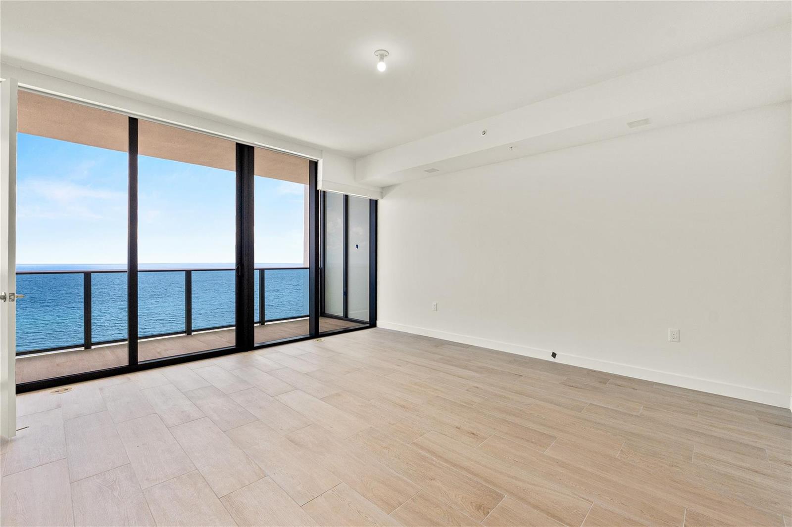 An empty room with light wood-look tile flooring and floor-to-ceiling windows overlooking the ocean — 900 N Ocean Boulevard # 1604, Pompano Beach FL 33062, POMPANO BEACH, FL