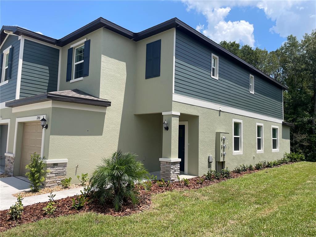 A two-story house exterior features light green stucco, dark blue siding, and a stone base — 17565 NECTAR FLUME DRIVE, LAND O LAKES, FL