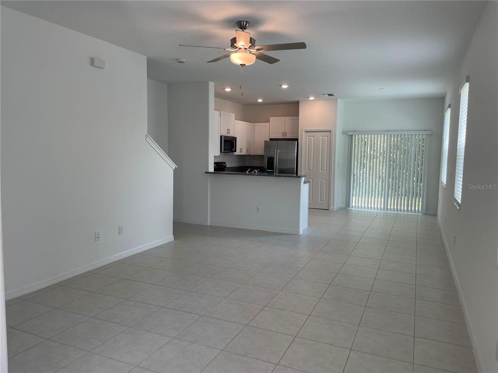 An open-concept living area features tile flooring, a kitchen with white cabinets, and sliding doors — 17565 NECTAR FLUME DRIVE, LAND O LAKES, FL