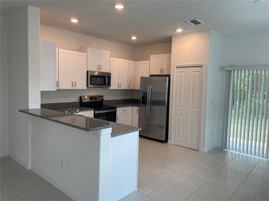 A kitchen features white cabinets, granite countertops, stainless steel appliances, and tile flooring — 17565 NECTAR FLUME DRIVE, LAND O LAKES, FL
