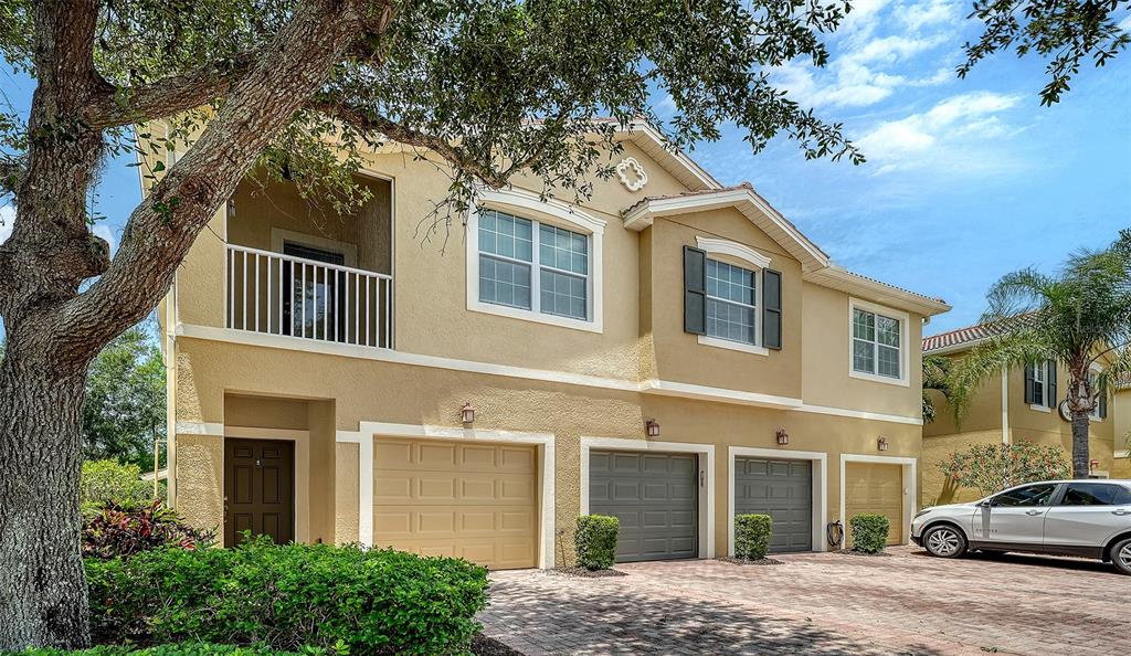 A two-story tan stucco townhouse features three garage doors and a second-floor screened balcony — 7843 MOONSTONE DRIVE UNIT 24-202, SARASOTA, FL