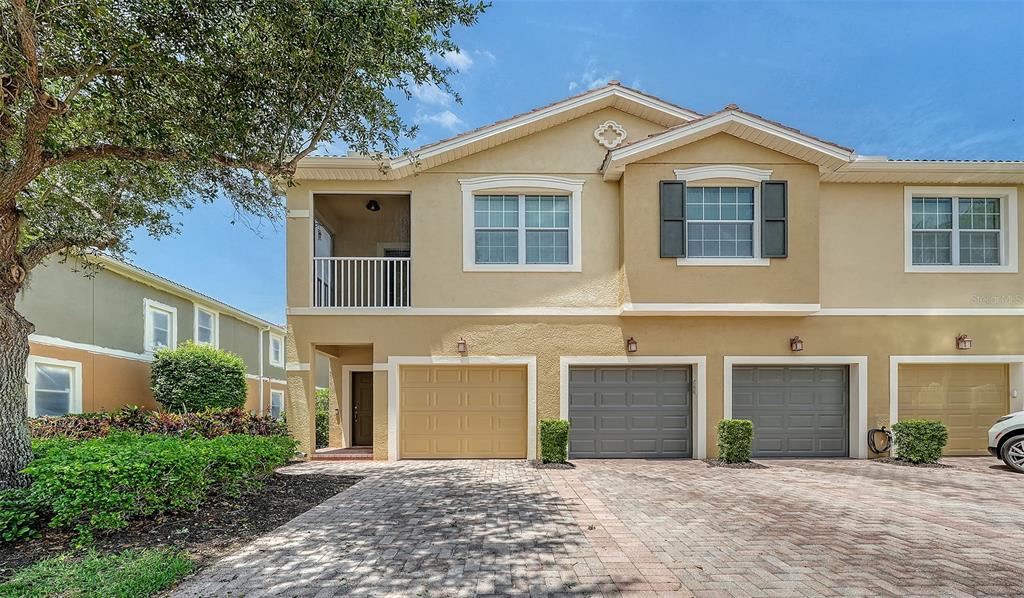 A two-story townhouse exterior features a tan stucco facade, three garage doors, and a balcony — 7843 MOONSTONE DRIVE UNIT 24-202, SARASOTA, FL